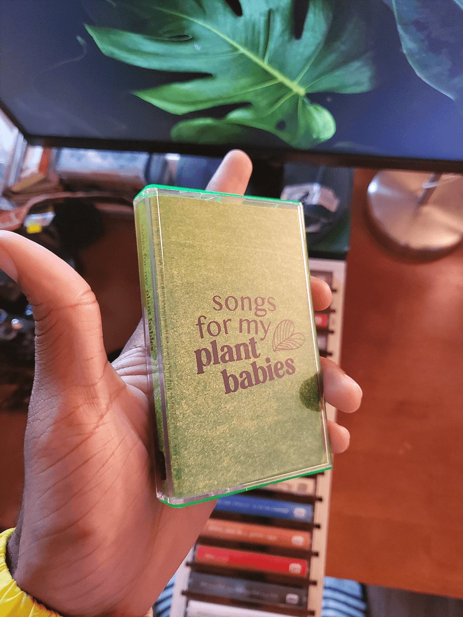 Songs for my plant babies in a green-tinted case, held in front of a monstera