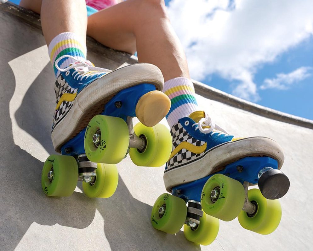 Blue and yellow checkered Vans roller skates with green wheels on a skate ramp