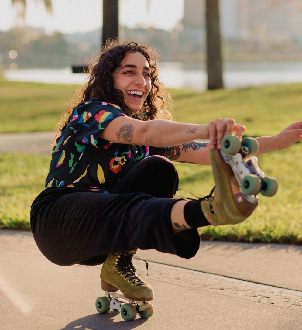 WOW Rolling’s owner laughing, crouched low on roller skates with one leg out, holding her skate